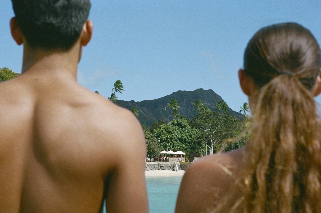 man and woman standing next to each other looking at the beach