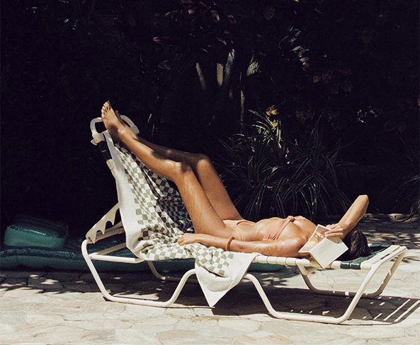 woman on a bikini laying on a sun bed with a towel and a book