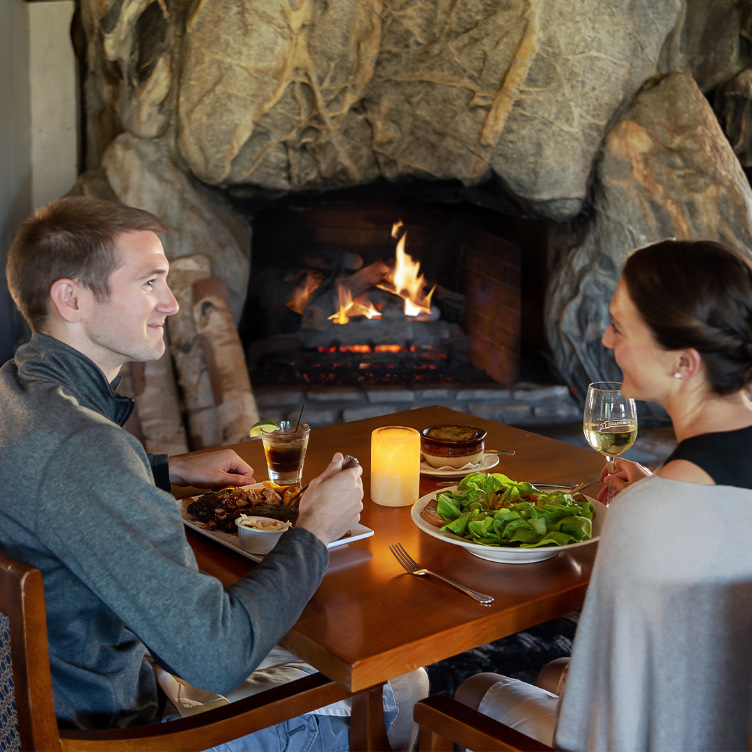 a man and woman sitting at a table with food and wine glasses