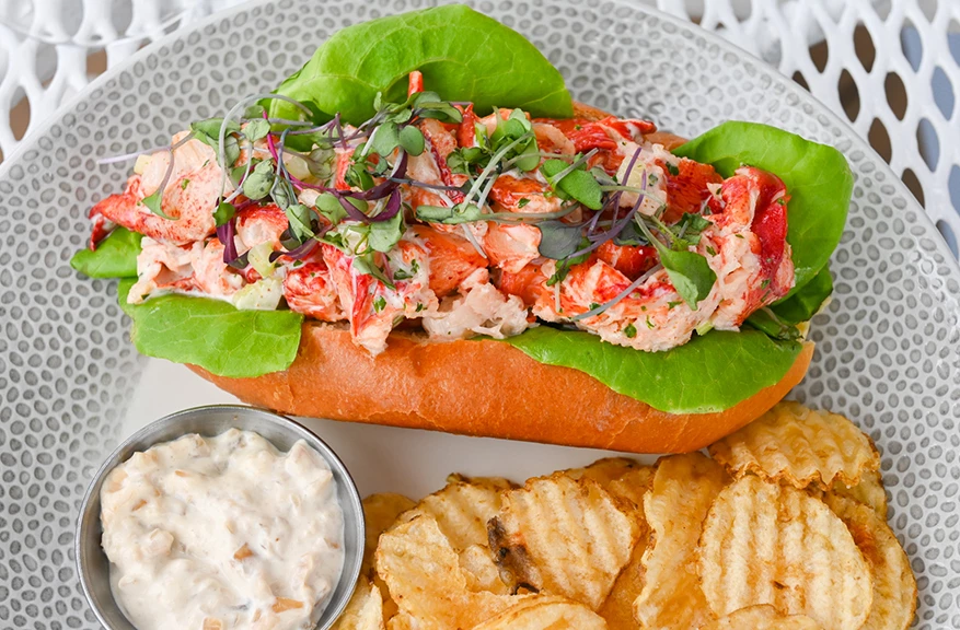 a lobster roll with lettuce and lettuce and a bowl of sauce