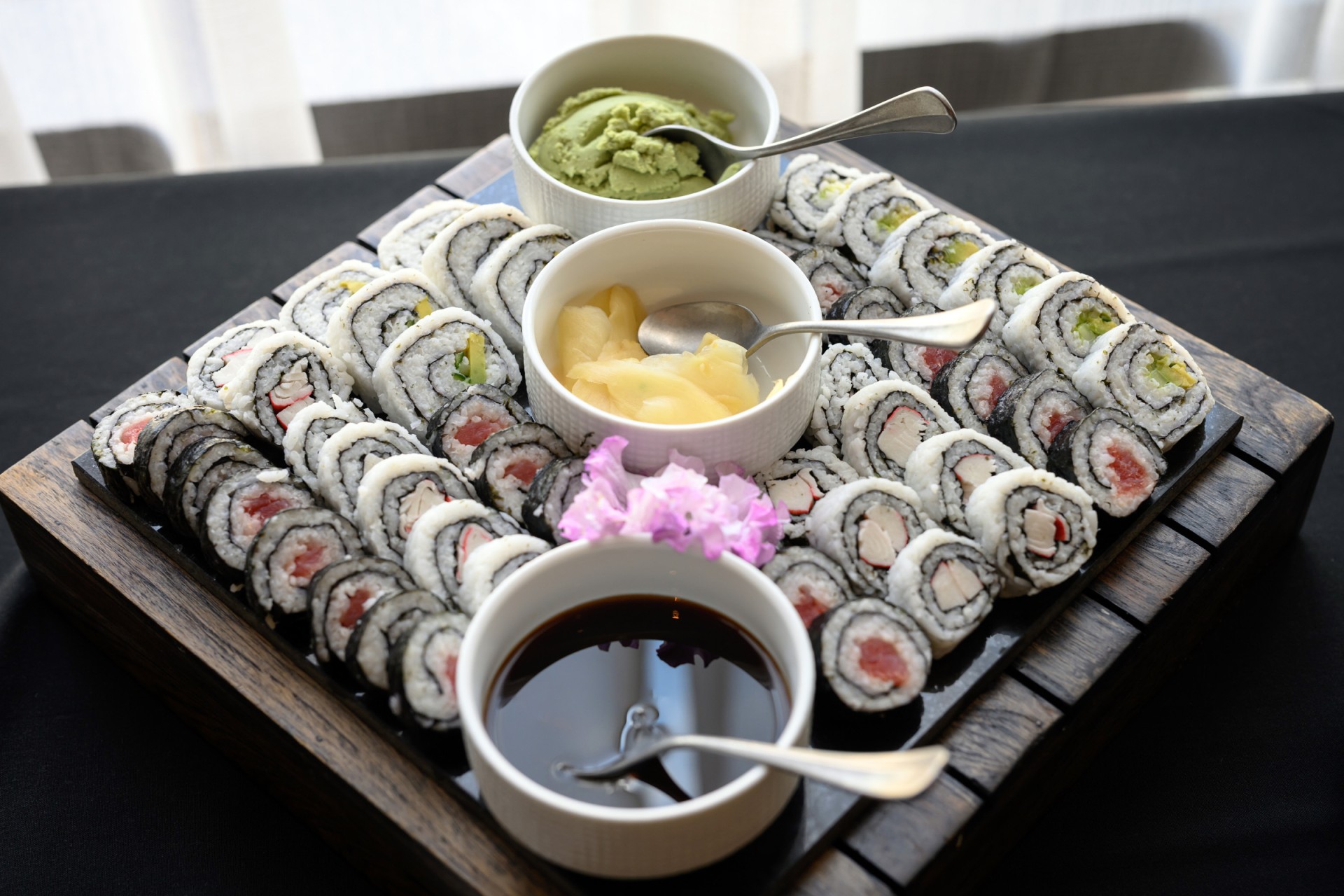 a tray of sushi with sauces and a flower
