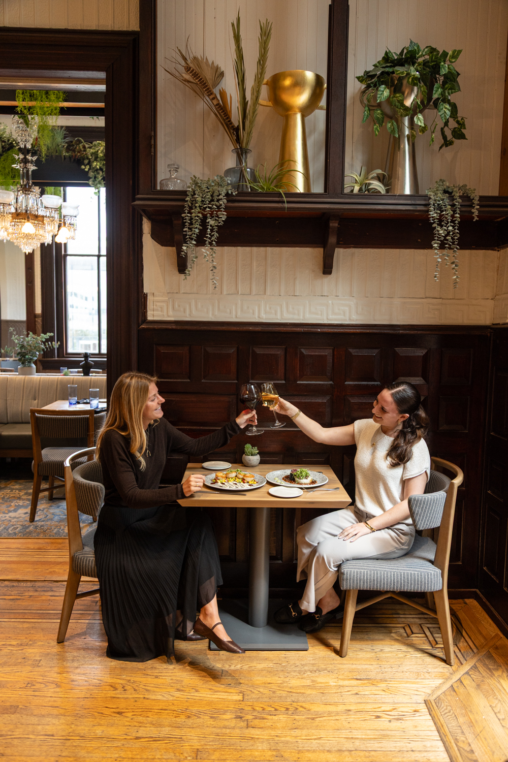 two women sitting at a table with food and wine glasses