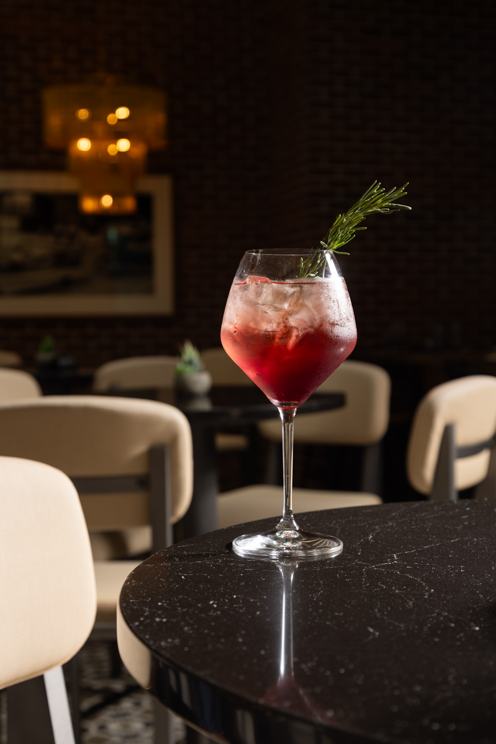 a glass of red liquid with a sprig of rosemary on a table