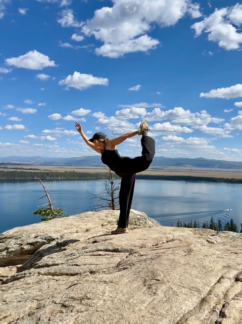 a woman standing on a rock with her leg up and a body of water in the background