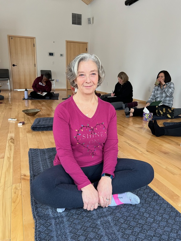 a woman sitting on a mat in a room with other people
