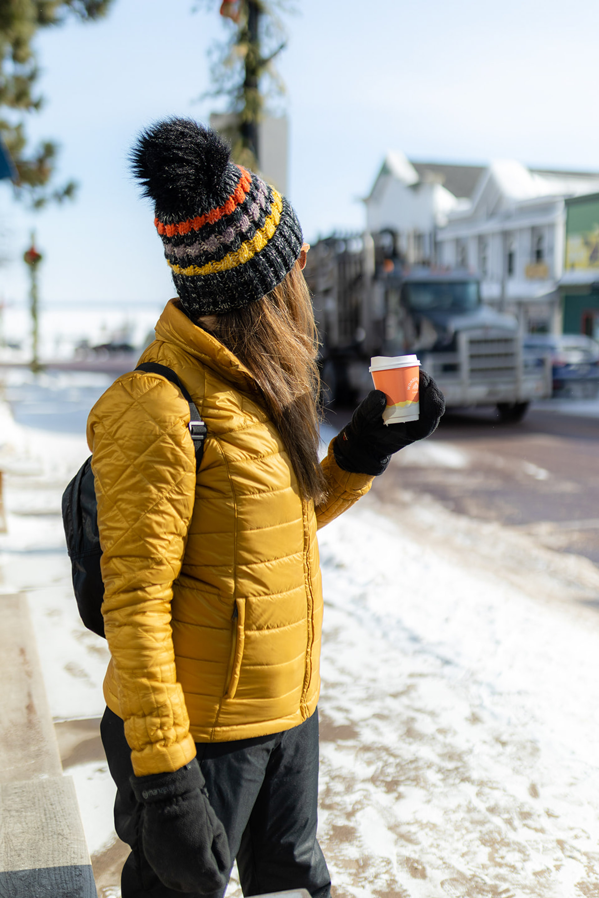 a woman wearing a yellow coat and knit hat holding a coffee cup