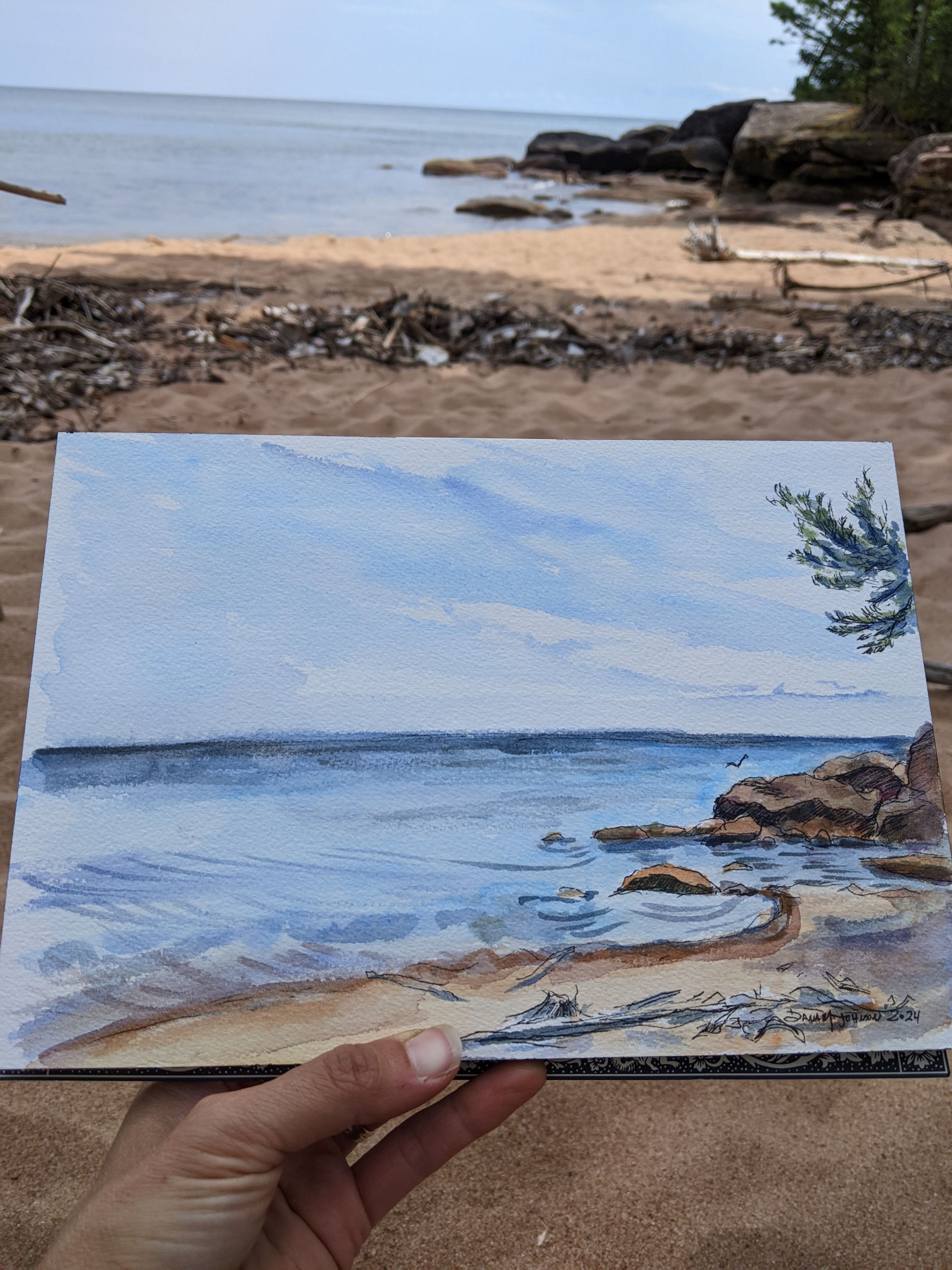 a hand holding a piece of art on a beach
