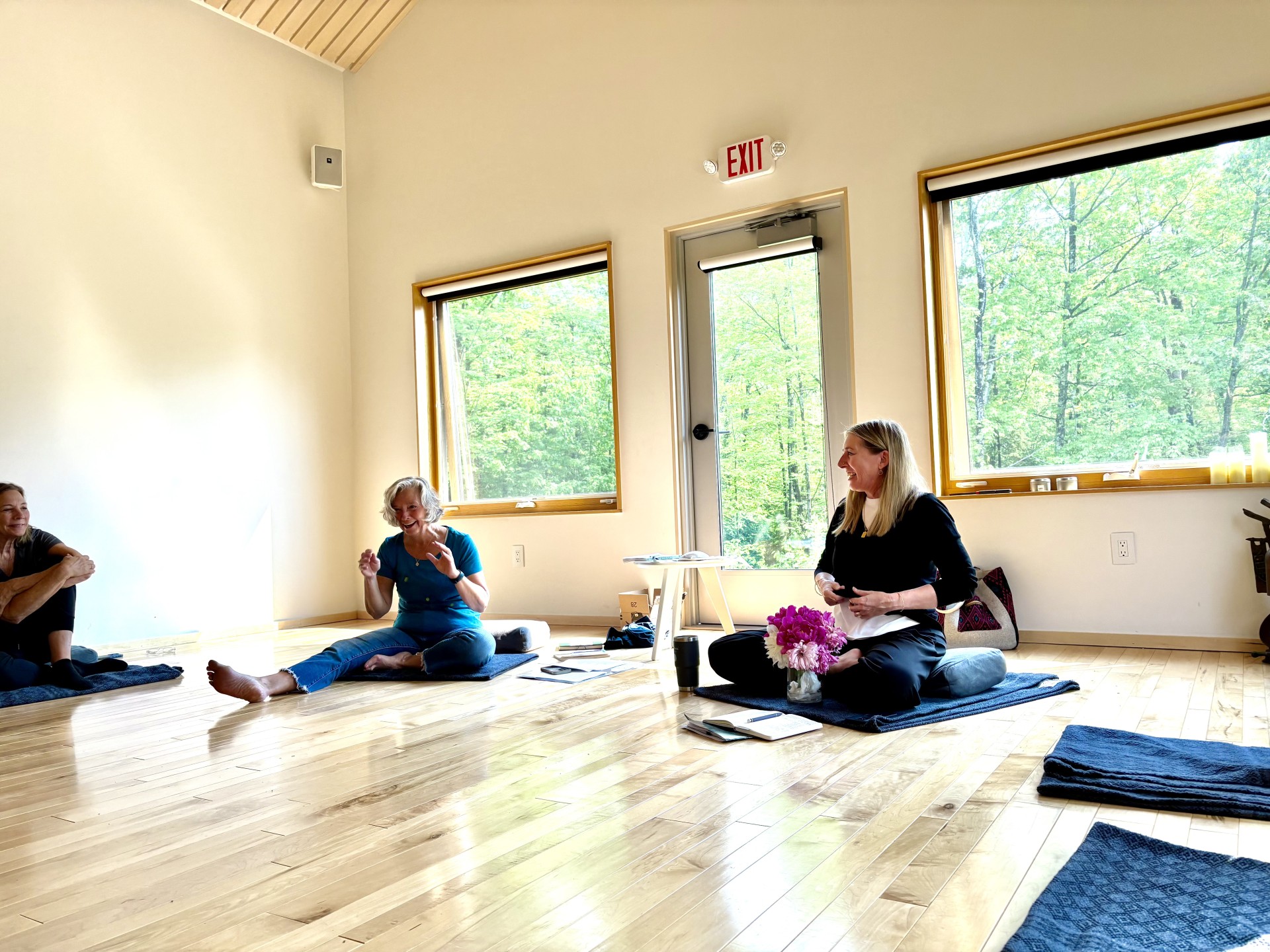 a group of women sitting on mats in a room with windows