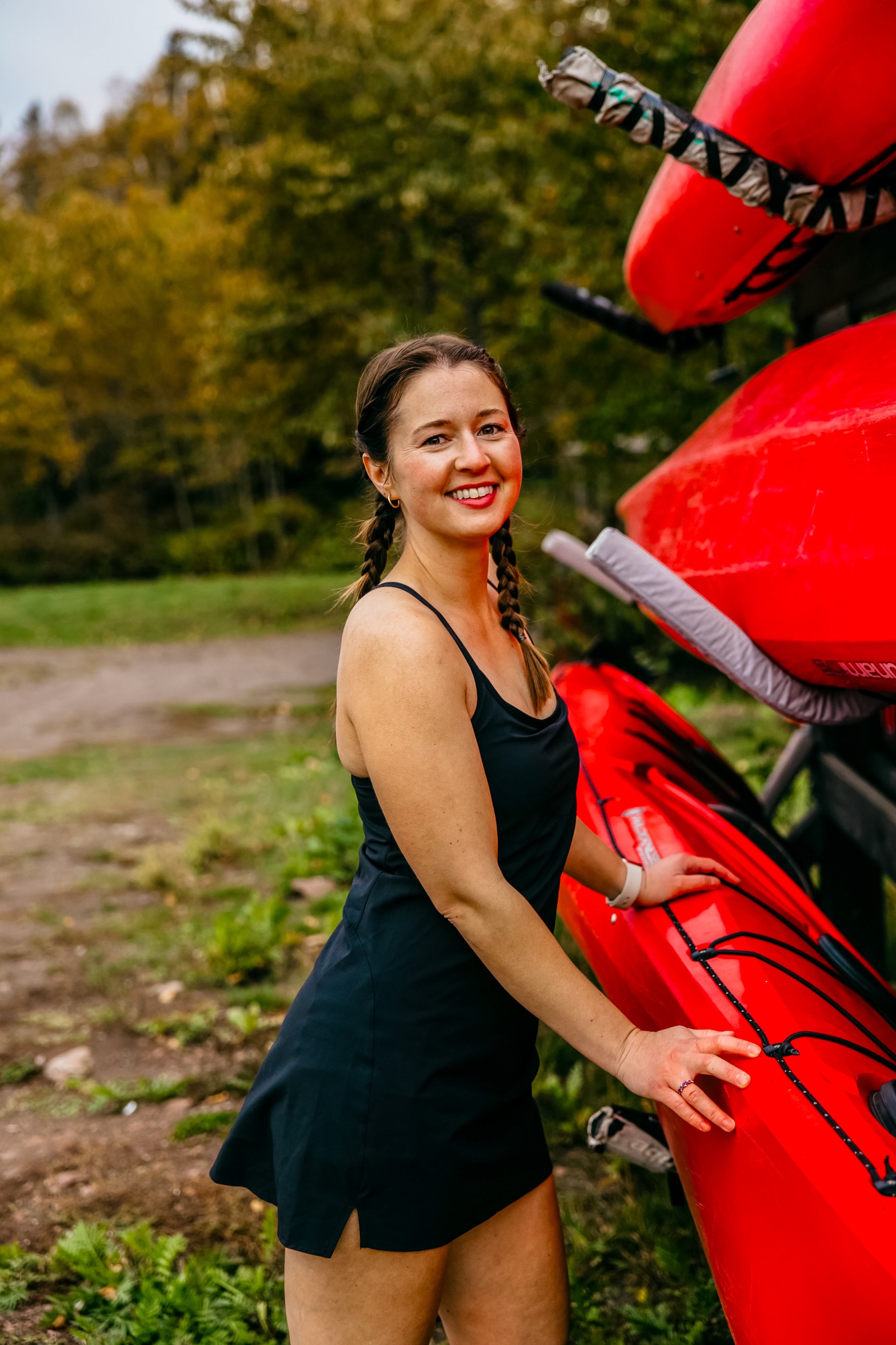 a woman in a black dress standing next to a red kayak