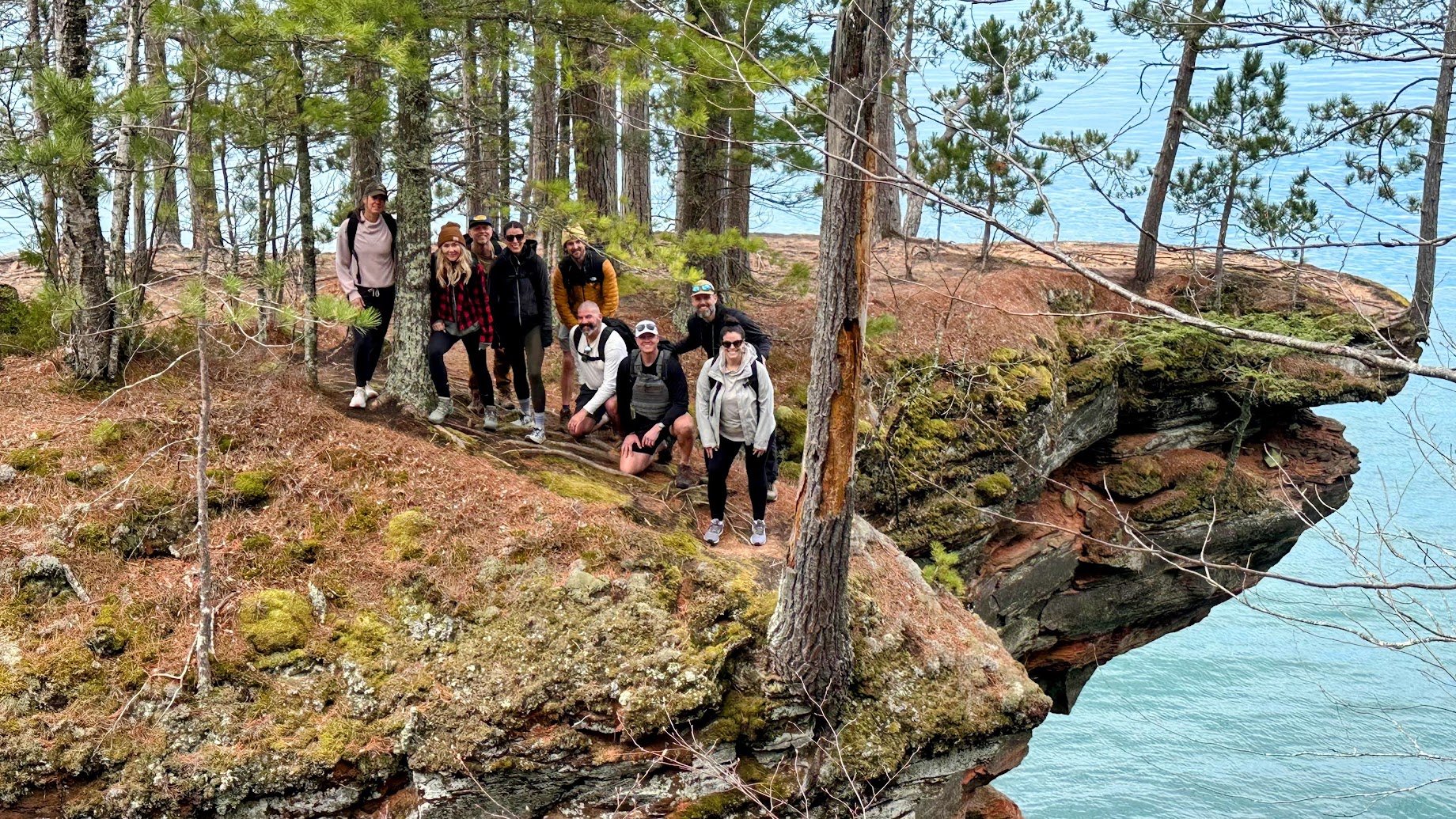 a group of people posing for a picture on a cliff above water
