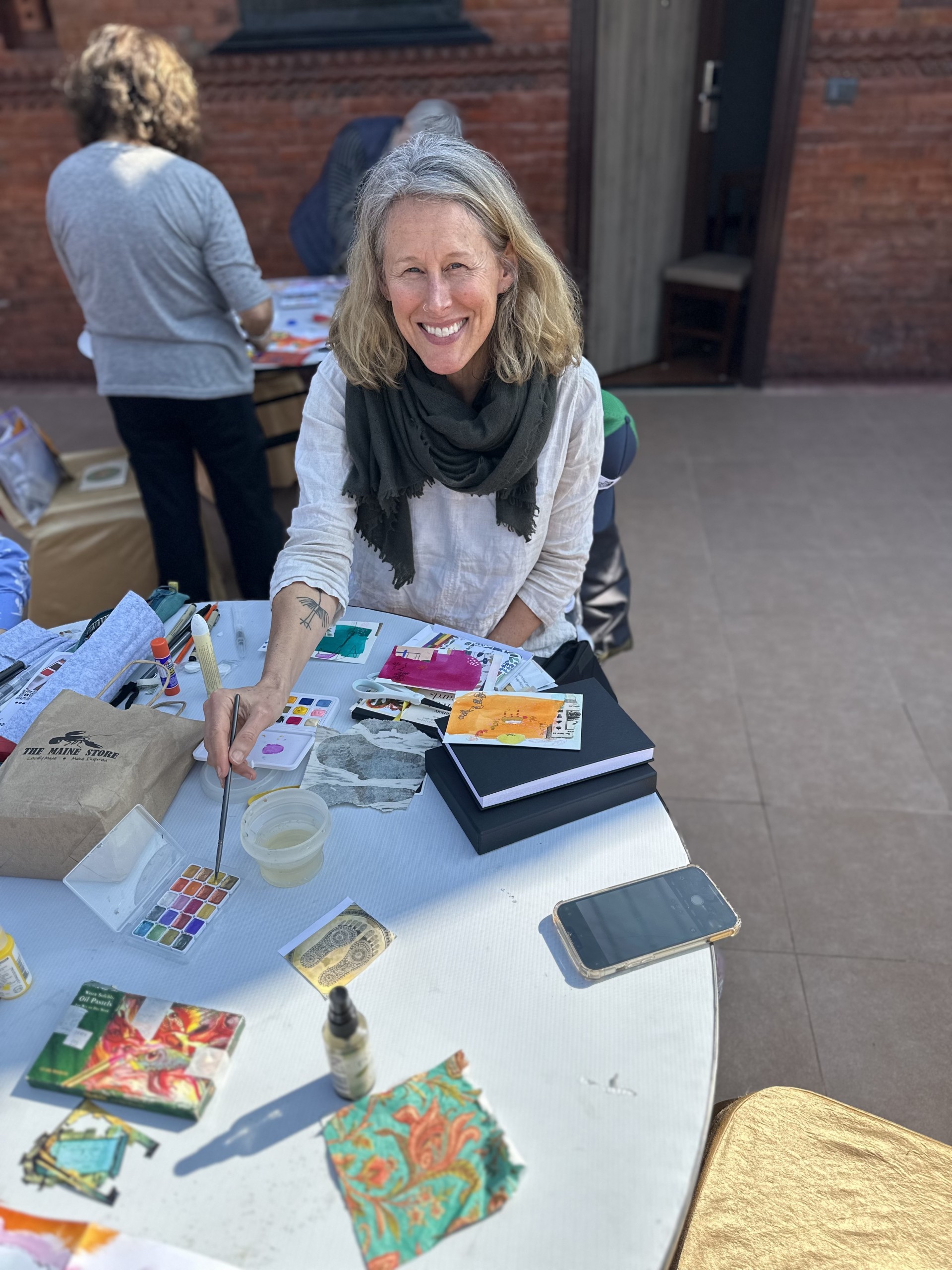 a woman sitting at a table with a paint brush