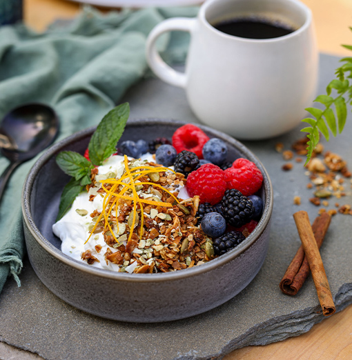 a bowl of fruit and yogurt with a cup of coffee