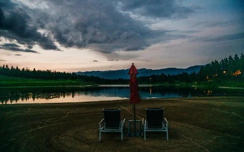 a couple of chairs and an umbrella on a grass field by a lake