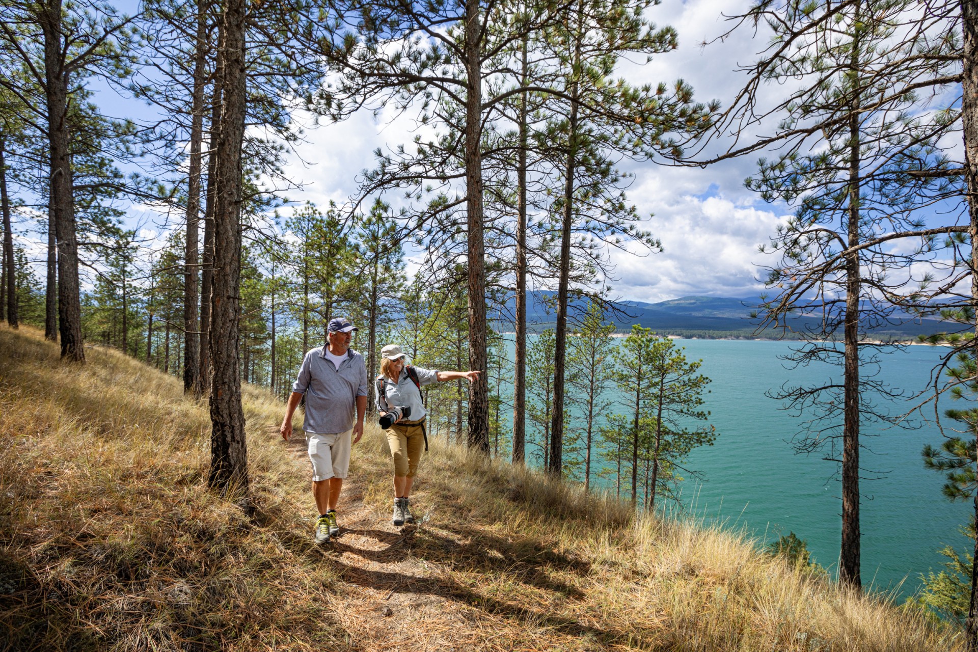 a man and woman walking on a trail with trees and water