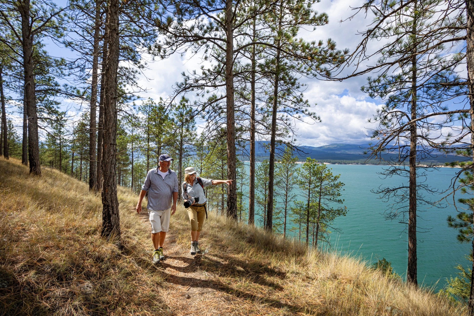 a man and woman walking on a trail with trees and water