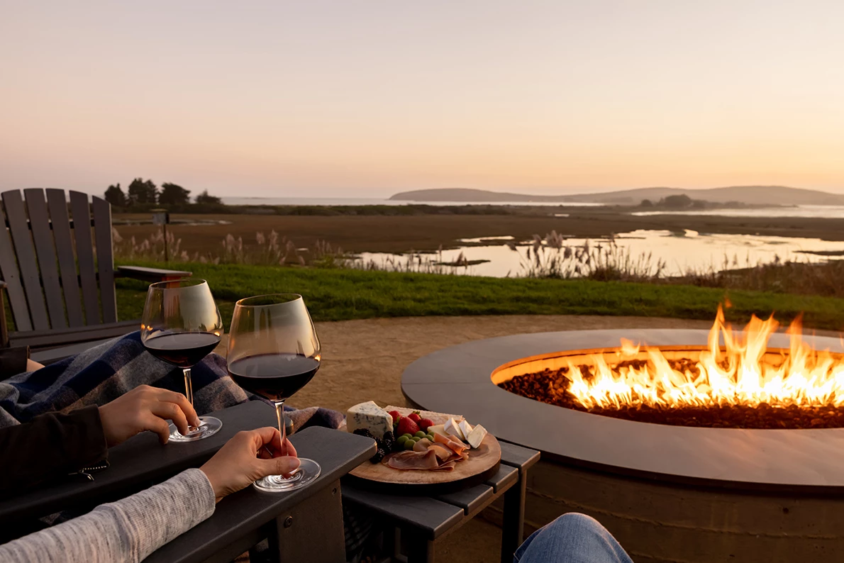 a couple of people sitting at a table with wine glasses and a fire pit