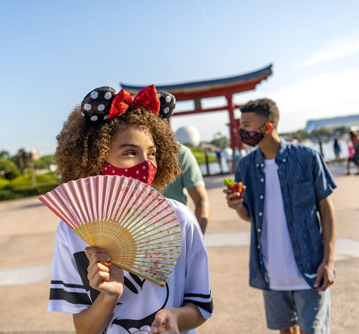 a girl holding a fan walking around Disney World's Epcot