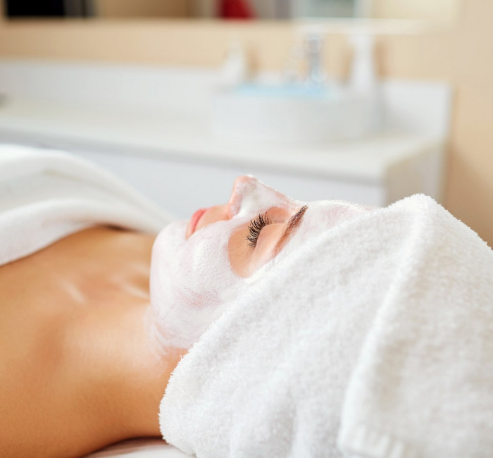 woman receiving a facial treatment with a white towel wrapped around her head