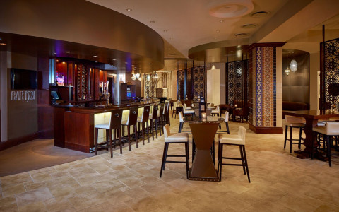 hotel bar area with curved wooden bar top and high-back white stools