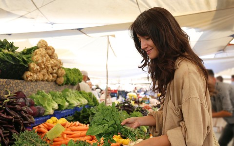 a woman standing in front of a market stall with vegetables