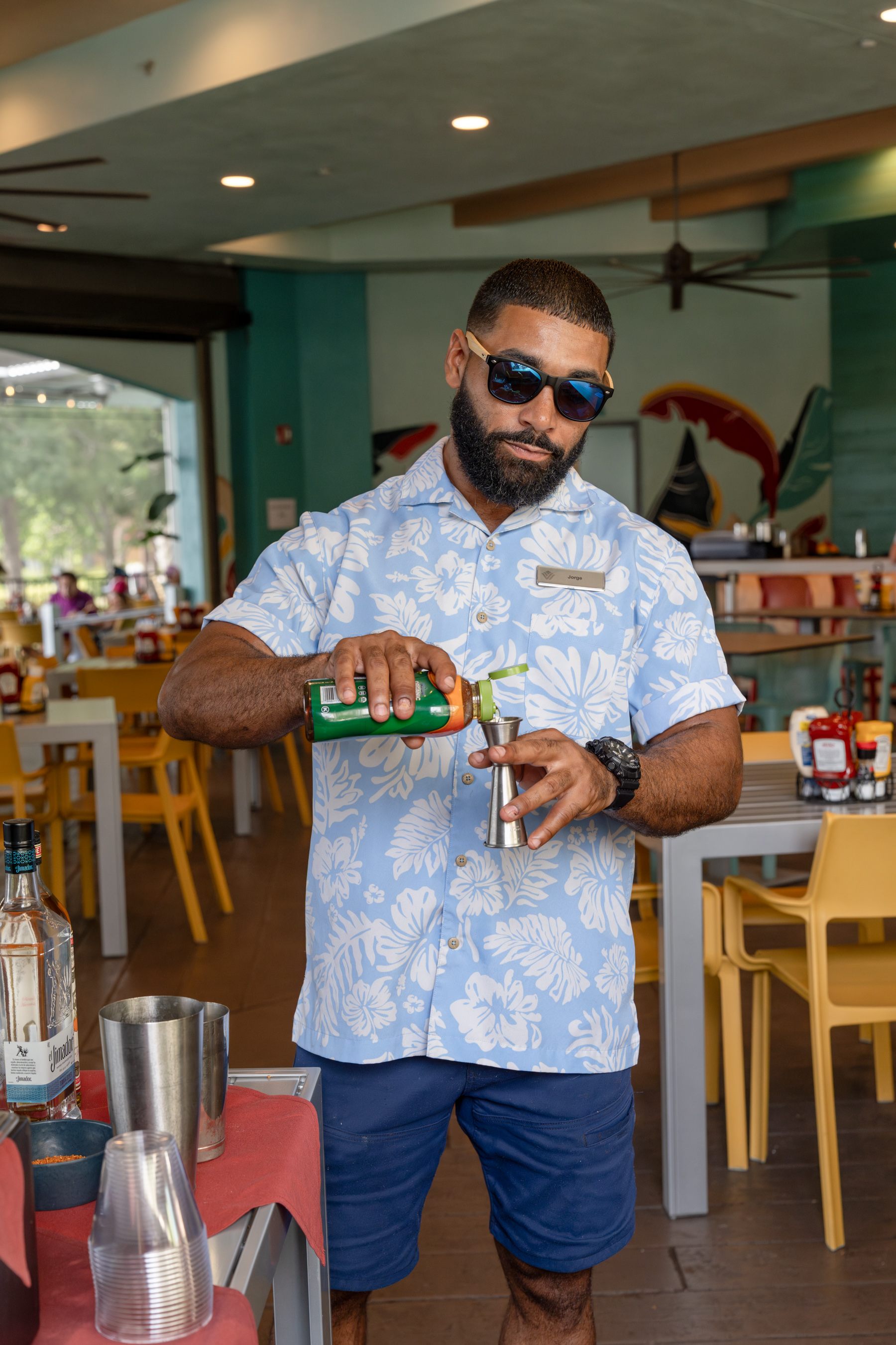 a man in a hawaiian shirt pouring a drink into a metal shaker