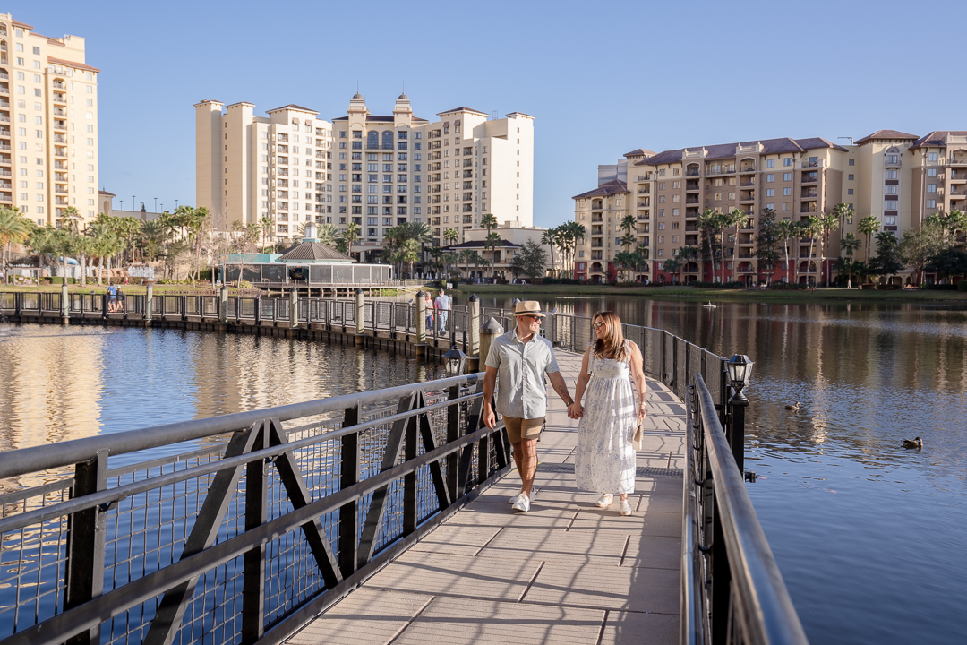 a man and woman holding hands on a bridge over water with buildings in the background