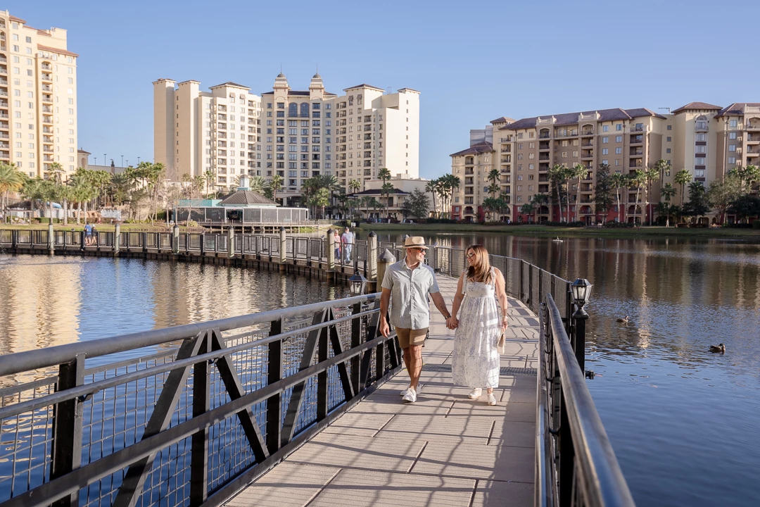 a man and woman holding hands on a bridge over water with buildings in the background