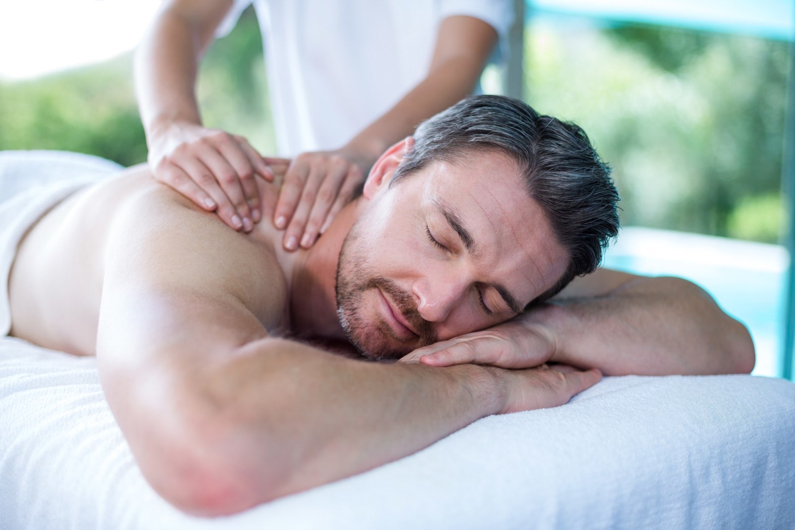 man with beard laying on table receiving a massage