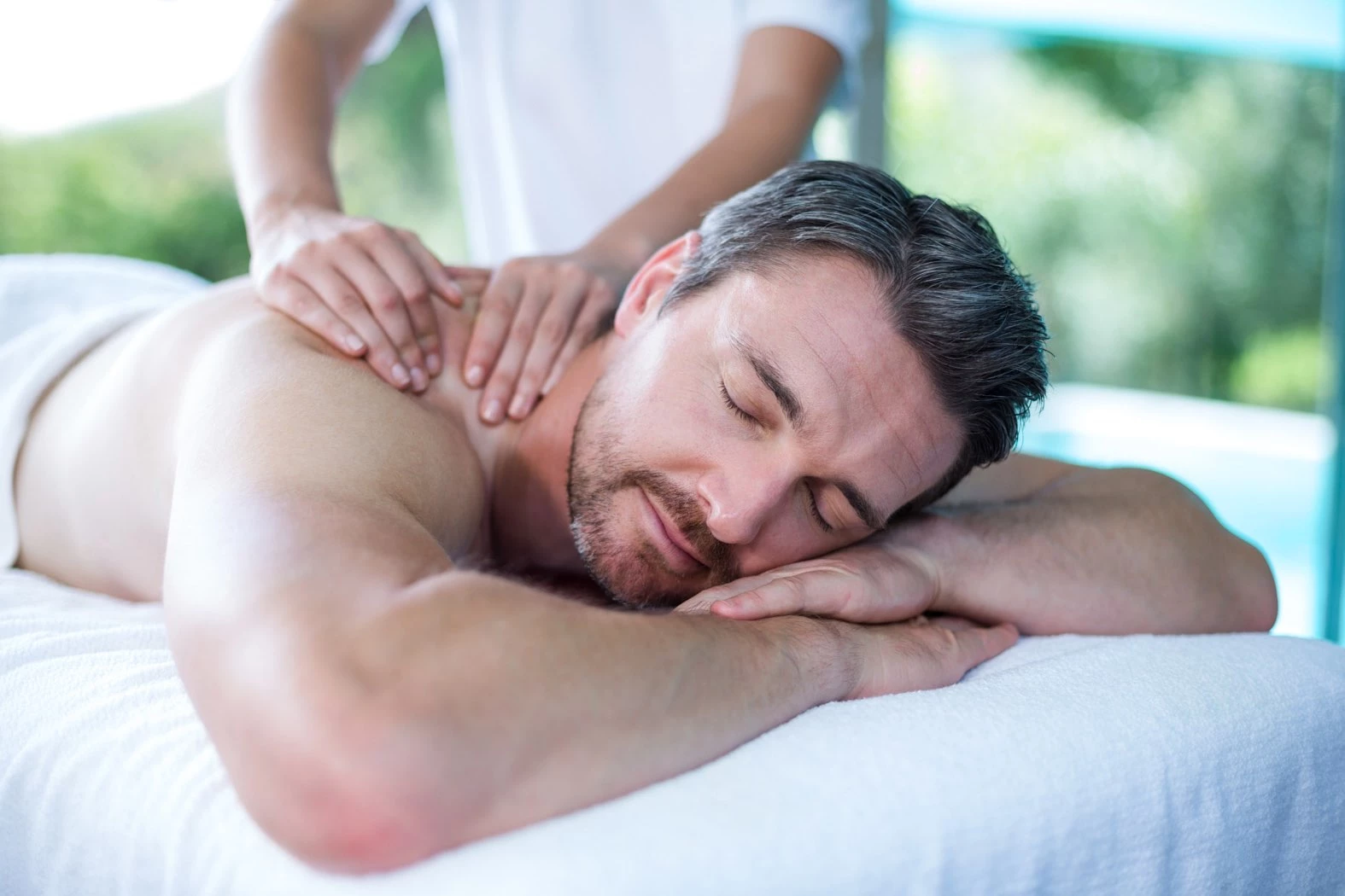 man with beard laying on table receiving a massage