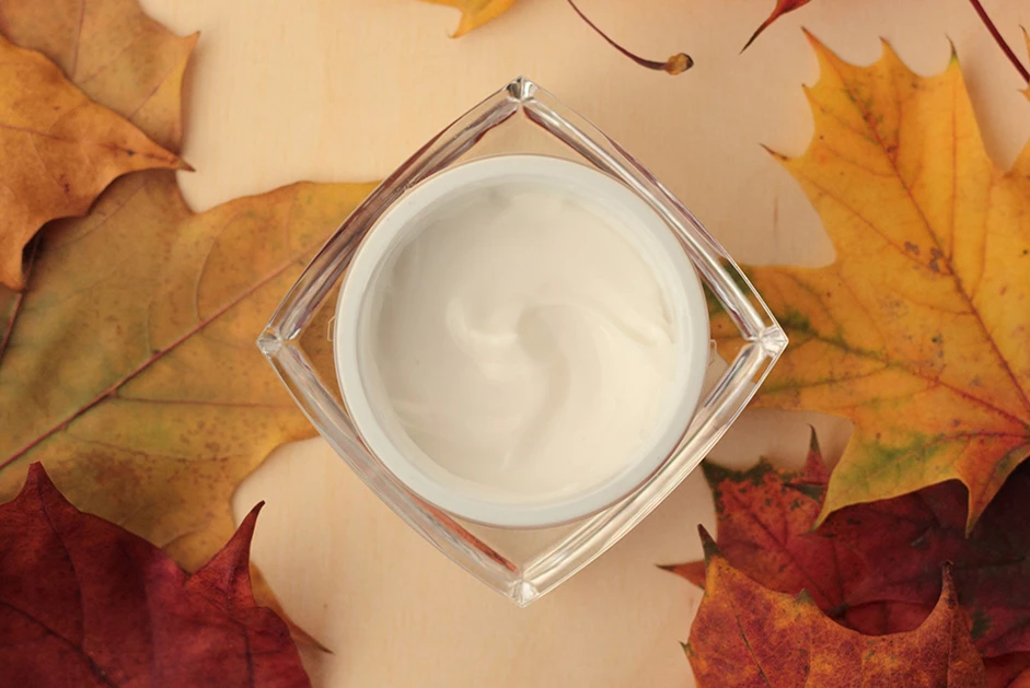 a jar of cream on a table with leaves around it