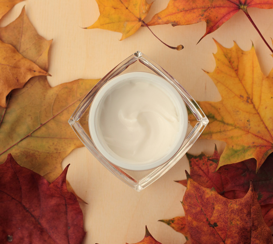 a jar of cream on a table surrounded by leaves