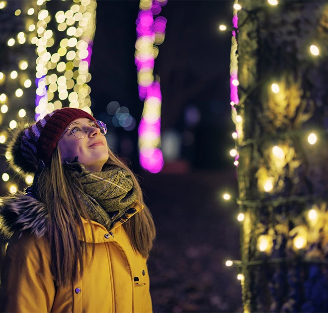 a woman in a yellow coat and hat outside with lights