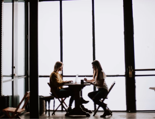 two women sitting down over coffee at table having a business meeting