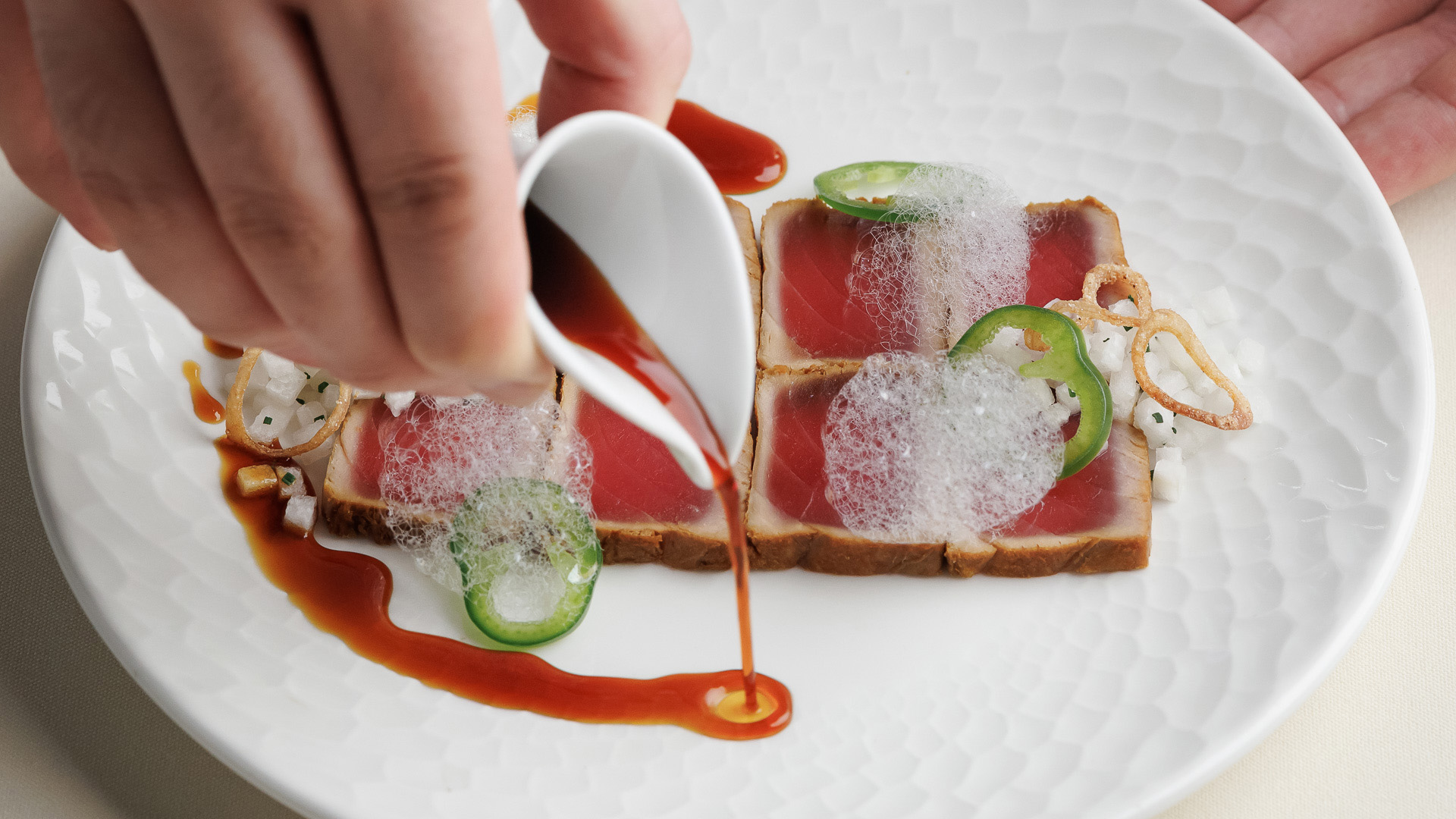 a person pouring sauce on food