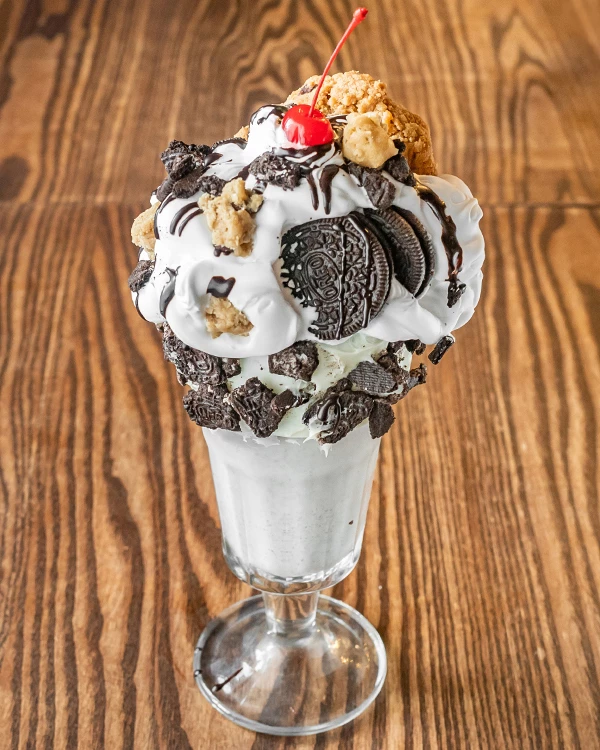 a glass with a milkshake with cookies and a cherry on top
