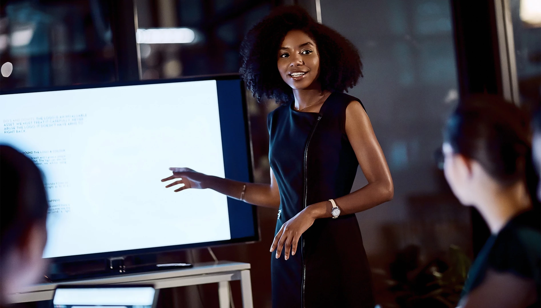 a woman in a black dress pointing at a screen