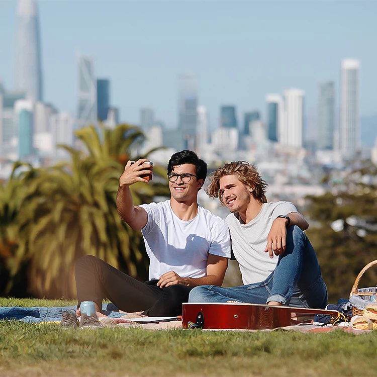 two men sitting on a blanket taking a selfie