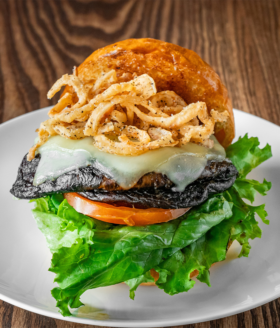 a burger with lettuce tomato and onion rings on a white plate