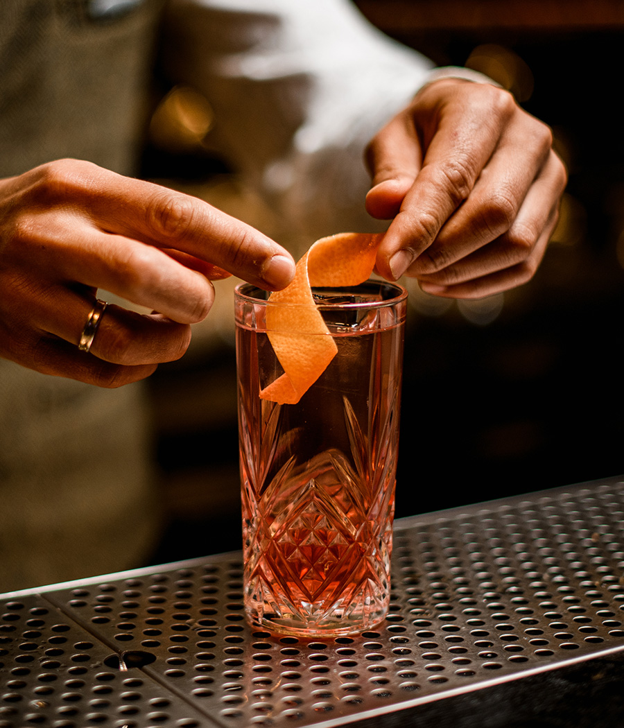 a person squeezing an orange peel into a glass of liquid