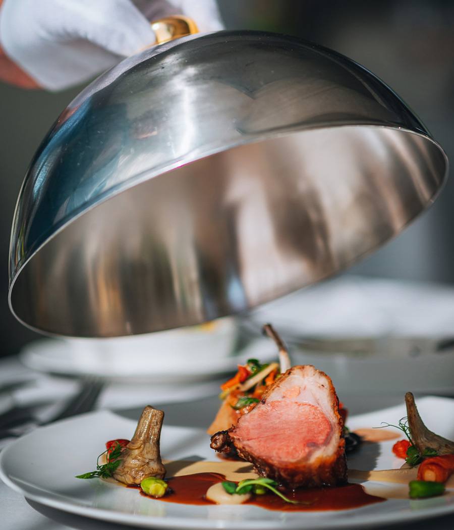 a chef holding a silver dome over a plate of food