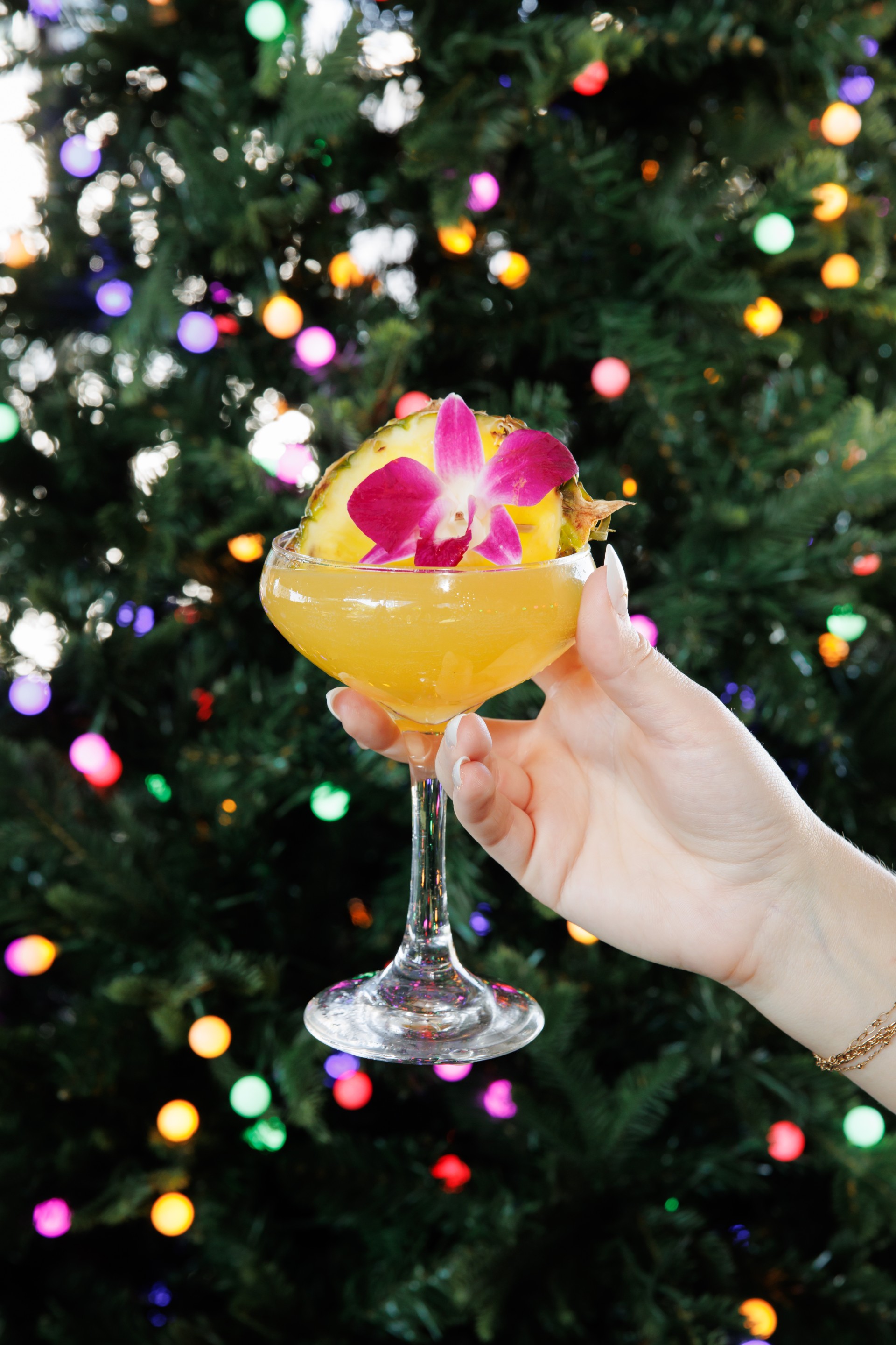 a hand holding a glass of yellow liquid with a flower on it