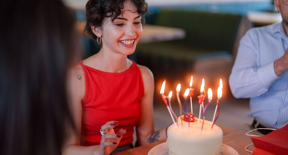 a woman smiling at a cake with candles