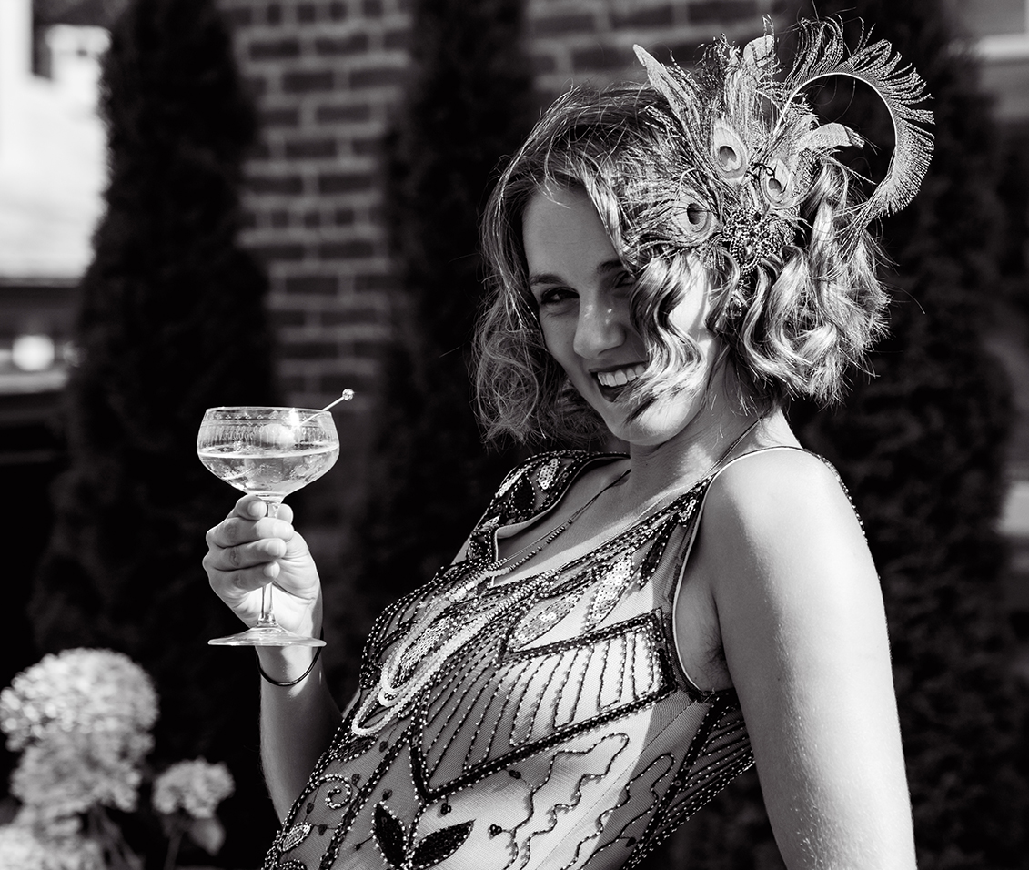 a woman wearing a feathered hat and holding a glass of wine