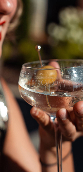 a hand holding a glass with liquid and a olive in it