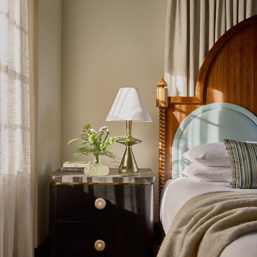 a bed with a lamp and a vase of flowers on a table