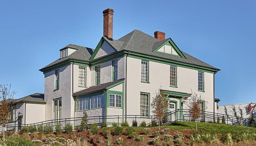 a large white and green house with a fenced yard