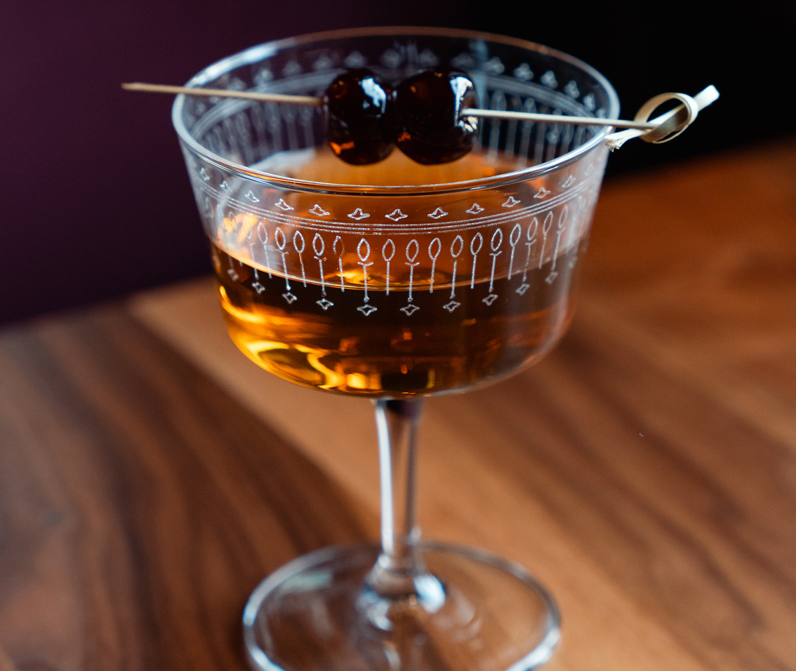 a glass with brown liquid and two cherries on it