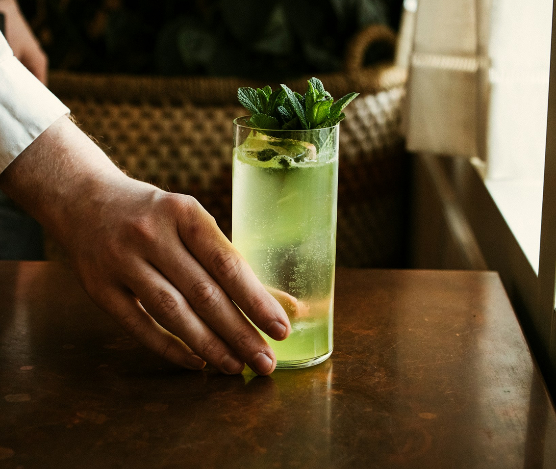 a hand holding a glass of liquid with mint leaves