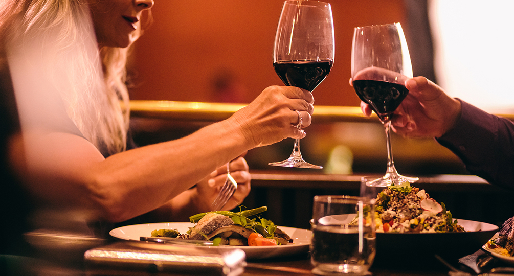 a woman holding wine glasses with a plate of food