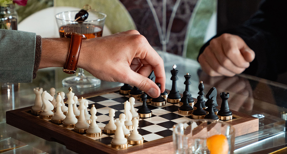 a hand playing chess with a glass of alcohol